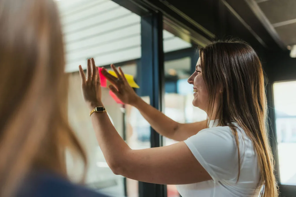 Collega plakt post-its op het raam tijdens een brainstorm